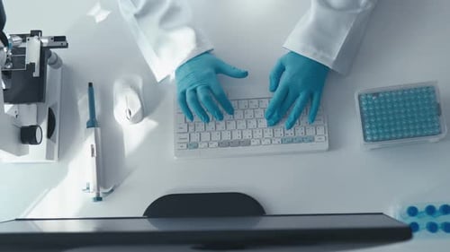 Person Typing at Laboratory Computer with Microscope