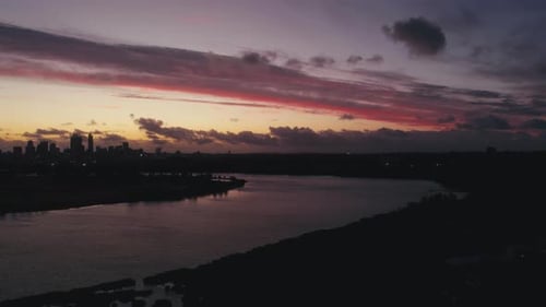 Atemberaubender Sonnenuntergang über der Skyline der Stadt, der sich in der Abenddämmerung auf ruhigem Wasser in der Nähe des Flussufers spiegelt