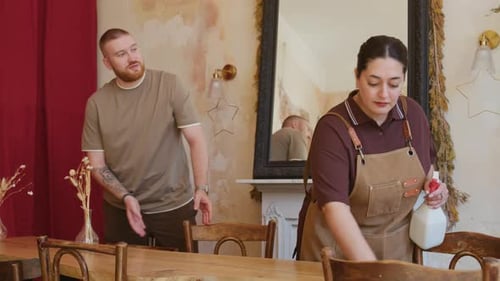 Male Manager Talking to Waitress Cleaning Tables before Cafe Opening