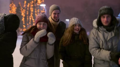 Friends Walking Under Snowfall on Christmas Market on Snowy Winter Night at Fairground Group of
