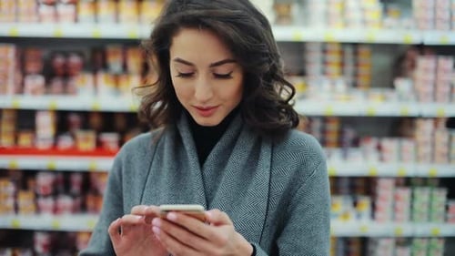 Happy Young Woman Use Phone in Supermarket Smiling Look at Camera Shopping Internet Buying