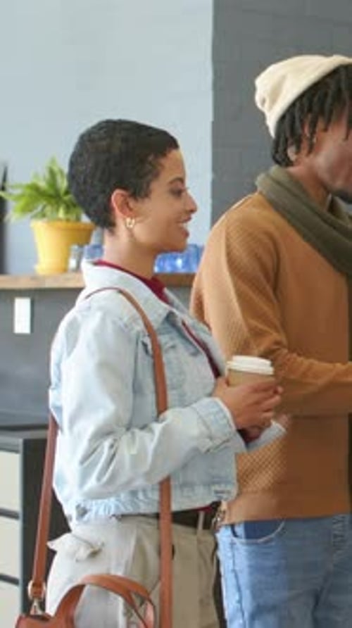 Vídeo vertical: mão estendida, mulher com bolsa e homem sorrindo no balcão do café, segurando copos para viagem