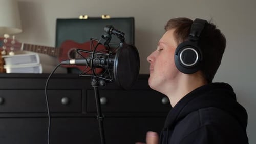 Young man recording vocals in a home studio, singing into a studio microphone with a pop filter