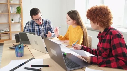 Young Adults Collaborate at Desks with Laptops