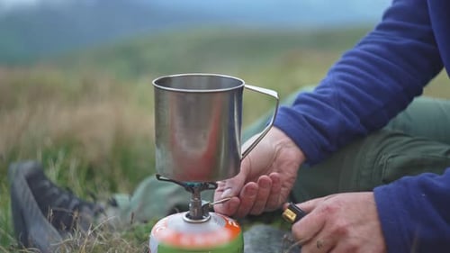 Man Prepares Hot Drink On Camping Stove Outdoors