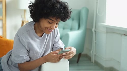 Afrikanisches Mädchen hält zu Hause Smartphone-Touchscreen in der Hand und tippt Scroll-Seite
