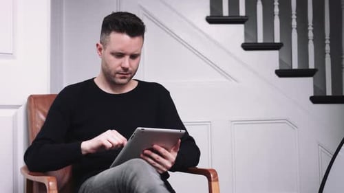 Man Sitting in Chair Using Tablet Indoors
