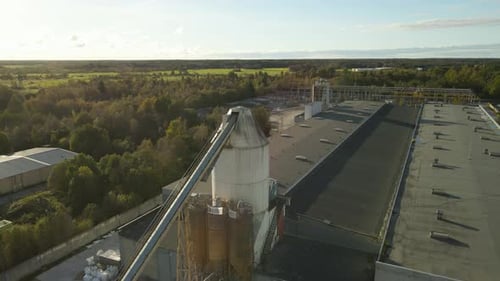 Aerial view of a concrete and cement factory tower in sunny countryside during summer day, trees.