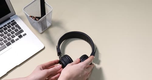 Woman putting headphones, smartphone, laptop and stationery on beige background, above view