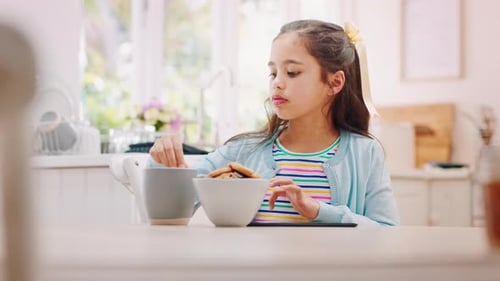 Girl Uses Tablet and Eats Cookies at Table
