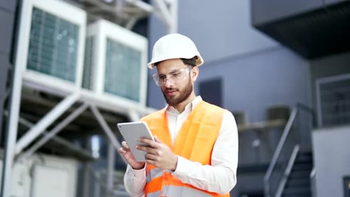 Professional engineer wearing safety helmet and vest standing at the factory and working