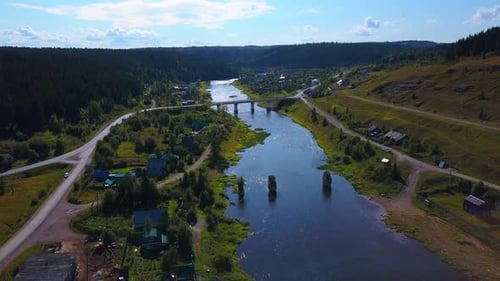Aerial view of a shiny river and a village surrounded by green vegetation