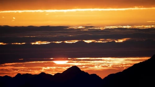 Silhouettes of mountains in golden sunset. Moving clouds in orange sky.