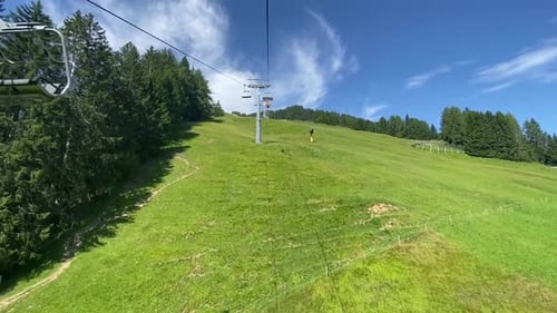 Ski Lift Ascending Green Mountain Slope on Sunny Day