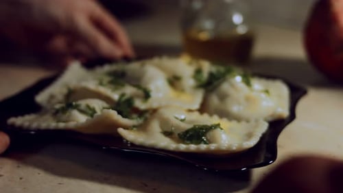 Closeup of Woman's Hands Rotating a Plate with Hot Cooked Ravioli Covered with Melted Butter and