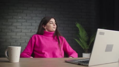 A Young Business Lady Finishes Typing and Sips Her Coffee A Brunette Girl in a Pink Sweater Works