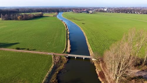Aerial view of a rural landscape with a canal curving through green fields, two small road bridges