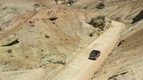 Large black SUV drives slowly and carefully down a dirt road cutting through the mountains in the Ra