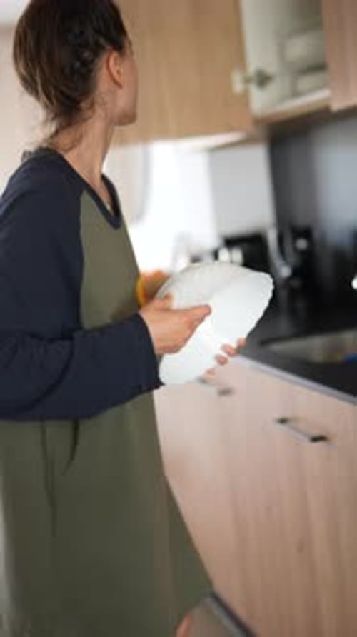 A Woman is Busy with Household Chores Unloading the Dishwasher and Storing Dishes in the Kitchen