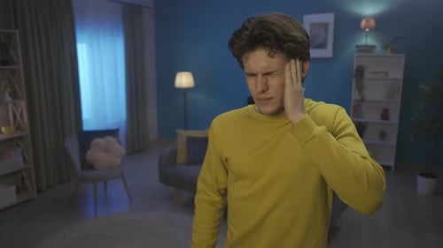 Unhappy Upset Man in the Living Room Massages His Temples Grimaces Suffering From a Severe Headache