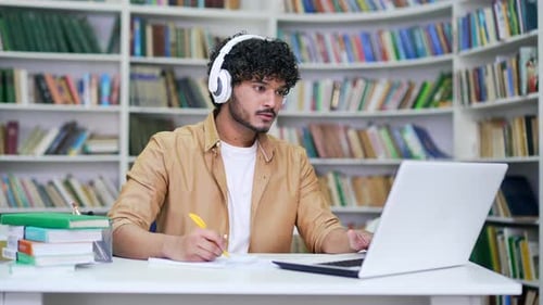 Young college student wearing headphones studying while watching online webinar, class webcast, look