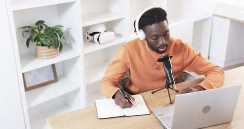 Ouvrant un ordinateur portable, un homme afro-américain prenant des notes, parlant au micro, partageant des idées au bureau à domicile