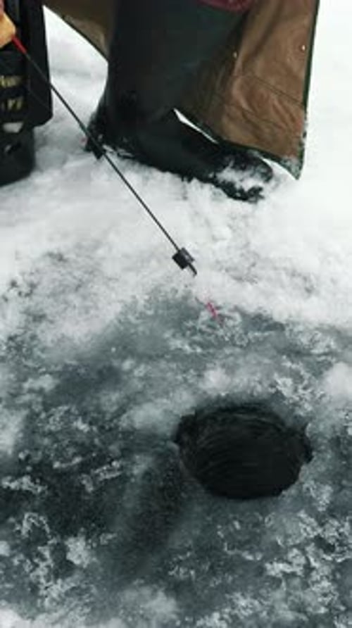 Close up of ice hole with fishing rod on frozen lake. Vertical video