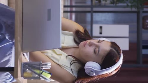 Vidéo verticale d'une étudiante écoutant de la musique et étudiant le soir.