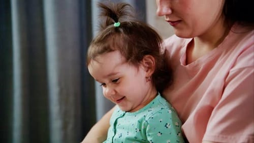 Smiling baby reading book with mother indoors