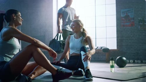Two Beautiful Fit Athletic Girls Sit on a Floor of Industrial Loft Gym. They're Happy with their Tr