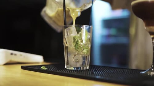 Close-up shot of a bartender making a glass of mojito on the bar, pouring in to the glass. Panning s