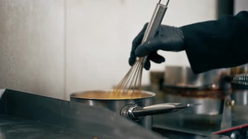 Nahaufnahme eines professionellen Küchenchefs in schwarzen Handschuhen kocht Käsesauce für Pasta