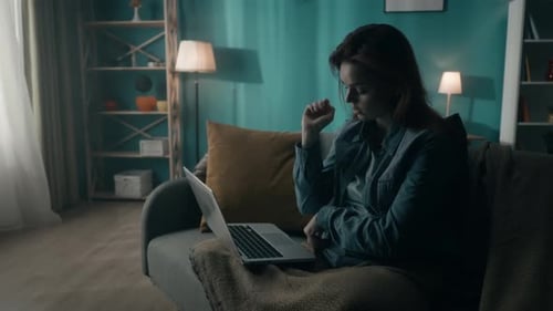 Tired Woman Working on a Laptop Studying Online While Sitting in a Room in the Dark Close Up