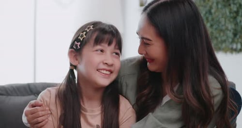 Affectionate Mother Hugging Adorable Daughter on Sofa