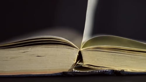 Slow motion, close up of an old, vintage, open book with pages turning on the wind, on a dark room w