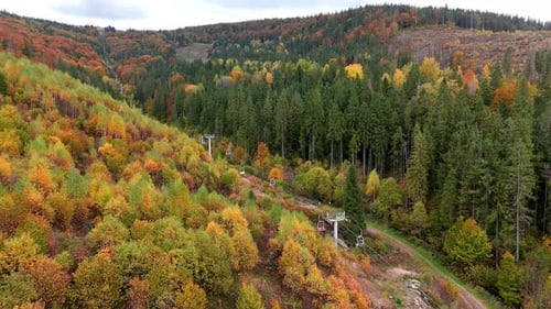 Aerial View of Ski Lift Moving Over Autumn Forest in Mountains Colorful Fall Trees on Hills