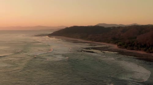 Aerial flight above breaking tidal swell on empty Costa Rica beach in sunset