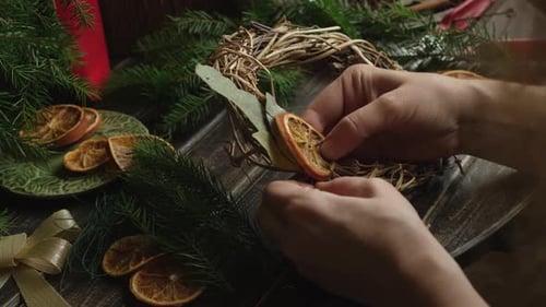 Hands Crafting Christmas Wreath with Ornaments and Greenery