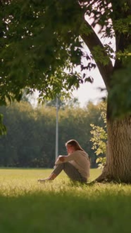 Thoughtful Woman Seated Under Tree in Serene Sunlit Park