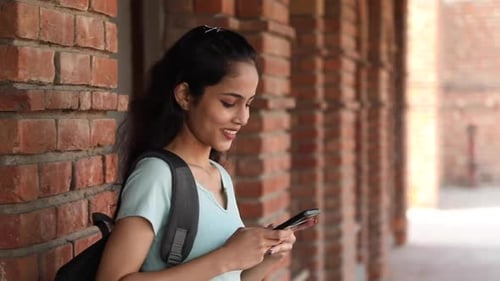 Video of a side view of a female college student typing text on her mobile phone on the college.