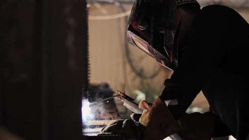 Man Welding Metal Structure in Dark Workspace