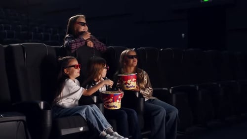 Four kids sitting in the cinema and eating popcorn