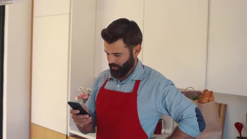 Portrait of Goodlooking Man with Beard Looking at Screen of Smartphone Likable Caucasian Man in Red
