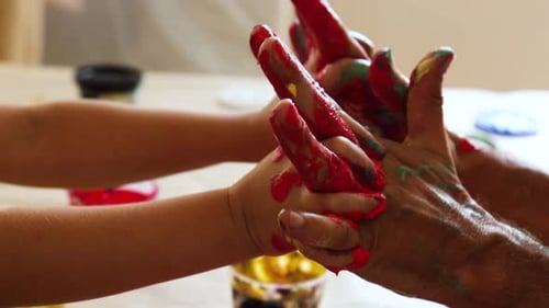 Intertwined hands and fingers of child and adult with red paint on them for connection and cooperati