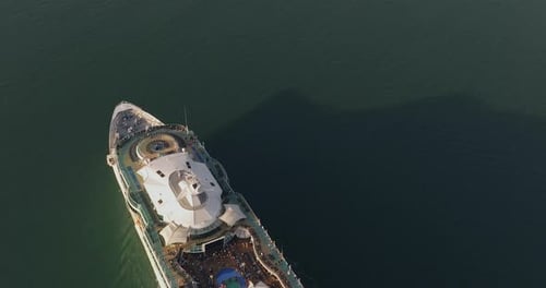 Large Cruise Ship with passengers on upper deck cruising at sea.