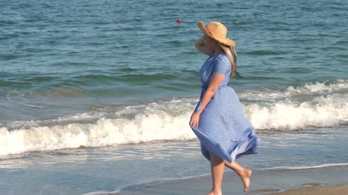 A Beautiful Young Woman with Long Blond Hair in a Long Blue Dress Walks Along the Beach Girl in a