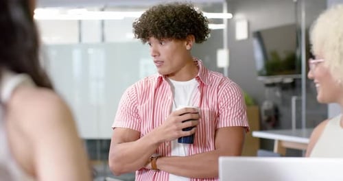 Holding coffee cup, man engaging in conversation with colleagues in office
