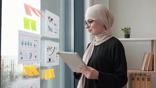 Woman Reviews Charts Using Tablet in Modern Office