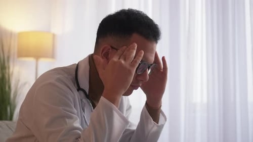 Stressed Doctor Indoors Holding Head in Hands