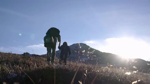 Cinematic shot of child and grandfather hiking in mountain during crisp and sunny autumn morning